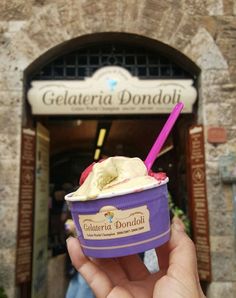 a hand holding up an ice cream sundae in front of a stone building with a doorway