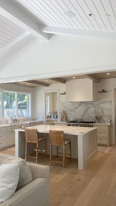 an open kitchen and living room area in a house with white walls, wood flooring and large windows