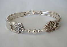 a silver bracelet with flowers and beads on the clasp is sitting on a white surface