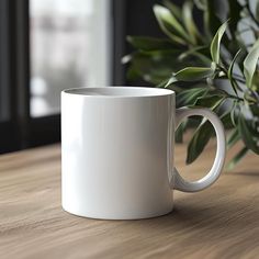 a white coffee mug sitting on top of a wooden table next to a potted plant