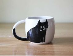 a black cat mug sitting on top of a wooden table