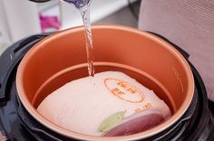 a person pouring water into an orange pot filled with meat and veggies in it