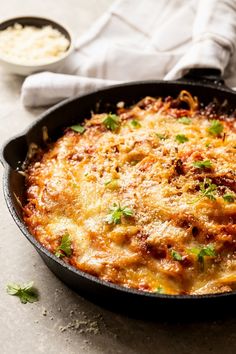 a casserole dish with cheese and vegetables in it on a table next to a white napkin