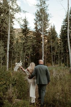 a bride and groom walking through the woods