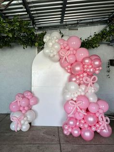 pink and white balloons are arranged in the shape of an arch with bows on it