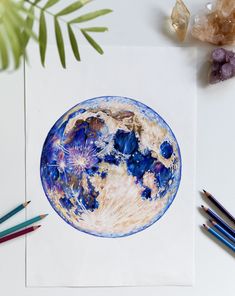 a drawing of the earth on paper with colored pencils next to it and some plants