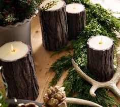 some candles are sitting on the table with deer antlers and greenery around them