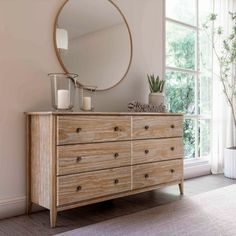 a wooden dresser with a round mirror on it's side next to a window