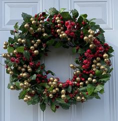 a christmas wreath is hanging on the front door with berries and greenery around it