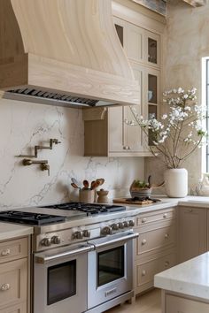 a kitchen with marble counter tops and stainless steel stove top oven, range hood, and white cabinets