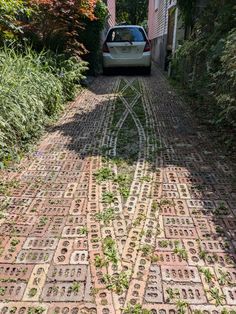 a car parked on the side of a road next to a brick walkway with grass growing all over it