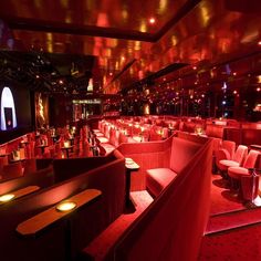 a dimly lit room with red lighting and couches in the center, along with tables and chairs