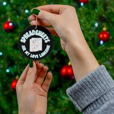 someone holding up a christmas ornament in front of a tree