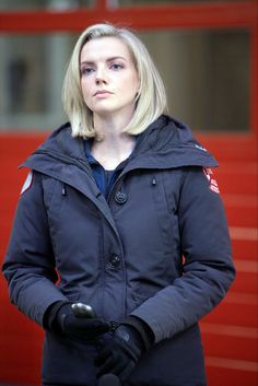 a woman standing in front of a red door with her hand on her hip and wearing black gloves