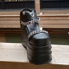 The Demonia Wave-20 Sandal In Black Vegan Leather Has A 3.25" Platform With A 6" Heel, Closed Toe Front, An Ankle Strap With Velcro Closure And Silver Moon, As Well As Attached Chain Hardware. #Demonia #Demoniawave #Demoniawave20 #Wave20 Shoes Demonia, Demonia Shoes, Black Platform Sandals, Black Vegan, Black Platform, Silver Moon, Platform Sandals, Black Silver, Ankle Strap