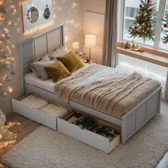 a bed with two drawers underneath it and christmas lights on the wall behind it in front of a window