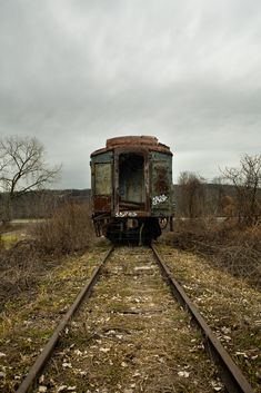 an old abandoned train car sitting on the tracks near some dead grass and trees with no leaves