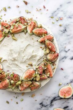 a cake topped with white frosting and sliced figs on top of a marble table