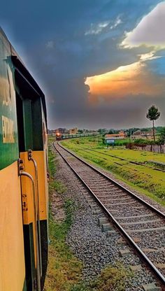 a train traveling down tracks next to a lush green field under a cloudy blue sky