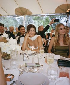 a group of people sitting at a table with plates and glasses on it, all smiling for the camera