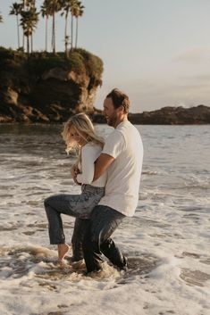 a man and woman are standing in the water at the beach with palm trees behind them