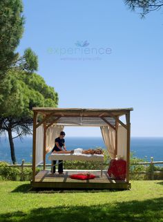 a man sitting on top of a bed under a canopy next to the ocean and trees