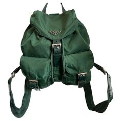 Prada vintage 1990's green nylon backpack. Features green canvas, leather details and silver buckles. Adjustable woven nylon straps, enamel metal triangle logo on the front flap, two small zip up pockets at the front and one inner zip pocket. Drawstring closure with flap and buckle. Brand: Prada Color: Green Material: Nylon. Leather Year / Season: 1990's Serial number: 104 Authenticity Guaranteed Measurements when laid flat: Length: 6 inches, Height : 12.5 inches Width: 12 inches, Tie Dye Bags, Ruffles Bag, Prada Backpack, Prada Vintage, Shoulder Backpack, Miuccia Prada, Lv Monogram, Triangle Logo, Nylon Backpack