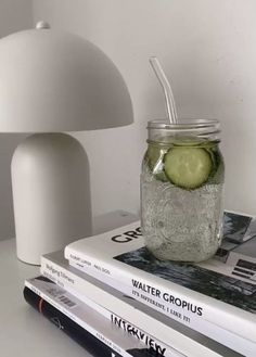 a mason jar filled with cucumbers sitting on top of books next to a lamp