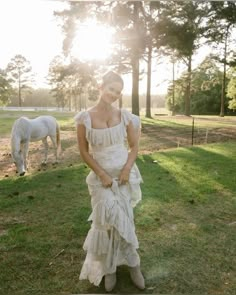 a woman in a white dress standing next to a horse