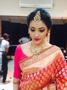 a woman in a red and gold sari with jewelry on her head, standing next to a table