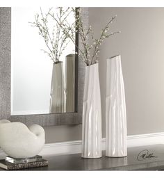 two white vases sitting on top of a table next to a mirror and planter