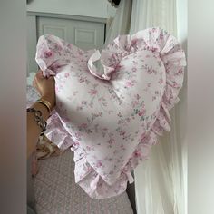 a pink heart shaped pillow sitting on top of a bed next to a white curtain