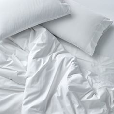 an unmade bed with white sheets and pillows