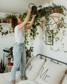 a woman is hanging plants on the wall above her bed while holding onto a hat