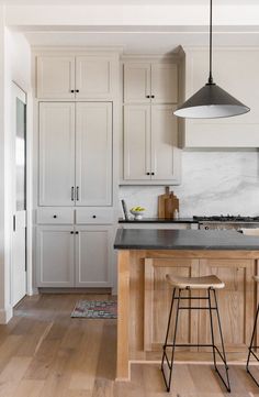 a kitchen with white cabinets and black counter tops, two stools in front of the island