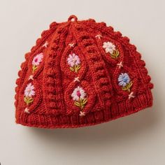 a red knitted hat with flowers and leaves on the front, sitting on a white surface