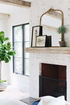 a living room with a fireplace, mirror and potted plant on the mantel