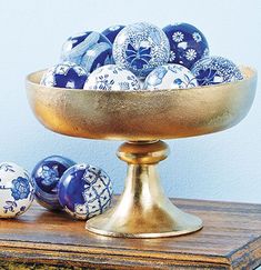 blue and white decorated eggs in a gold bowl on a wooden table next to other ornaments