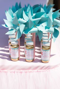 four jars with blue paper flowers in them sitting on a pink tablecloth covered table