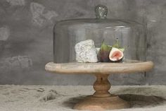 a figurine under a glass clochel on a wooden base with two pieces of fruit in it