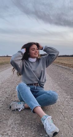 a woman sitting on the side of a road with her hands behind her head,