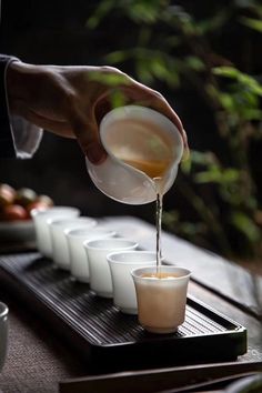 a person pours liquid from a pitcher into small cups