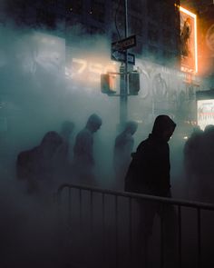 people are standing in the fog near a street sign and traffic light on a city street