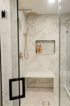 a bathroom with marble walls and flooring, including a white bench in the shower