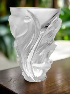 a white glass vase sitting on top of a wooden table next to a green plant