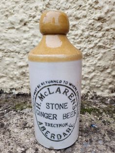 an old fashioned bottle is sitting on the ground next to a white wall and cement