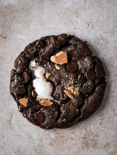 a cookie with chocolate chips and marshmallows on top, sitting on a gray surface