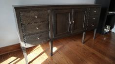 a wooden dresser sitting on top of a hard wood floor next to a white wall