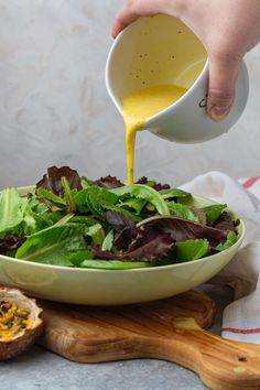 a person pouring dressing into a salad with lettuce and other greens in a bowl