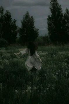 a woman in a white dress is running through the grass with her arms spread out